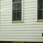 Power washing technician using wand to soft wash vinyl siding